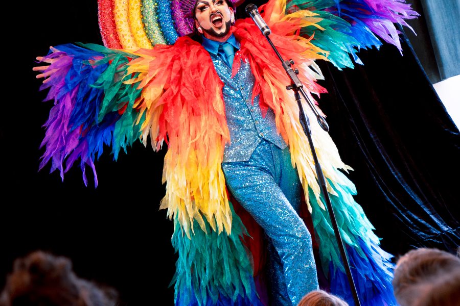 Performer in vibrant rainbow costume sings on stage, captivating a young audience.